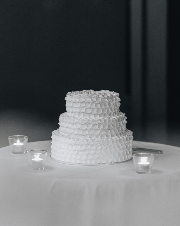 The wedding cake is an elegant 3 tiered cake, sitting on a round table with tealight candles