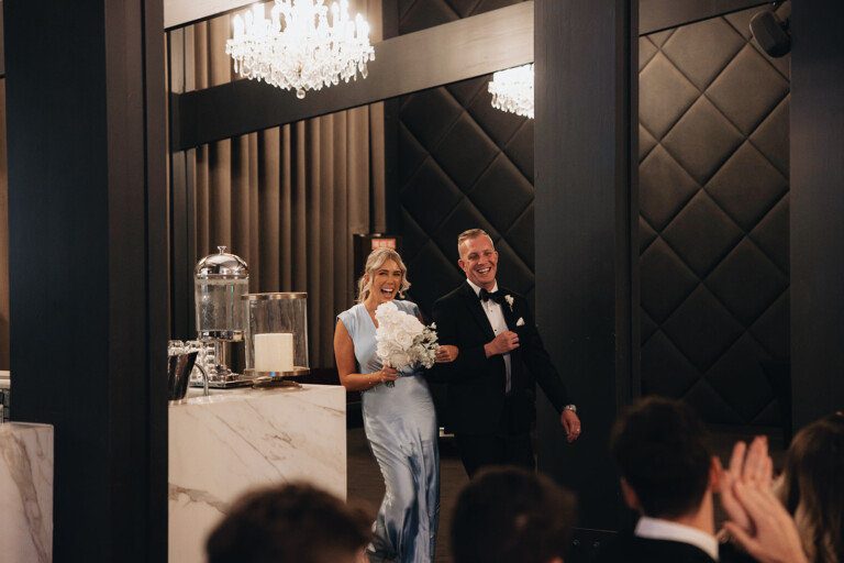 A bridesmaid and groomsman walks into the reception smiling.