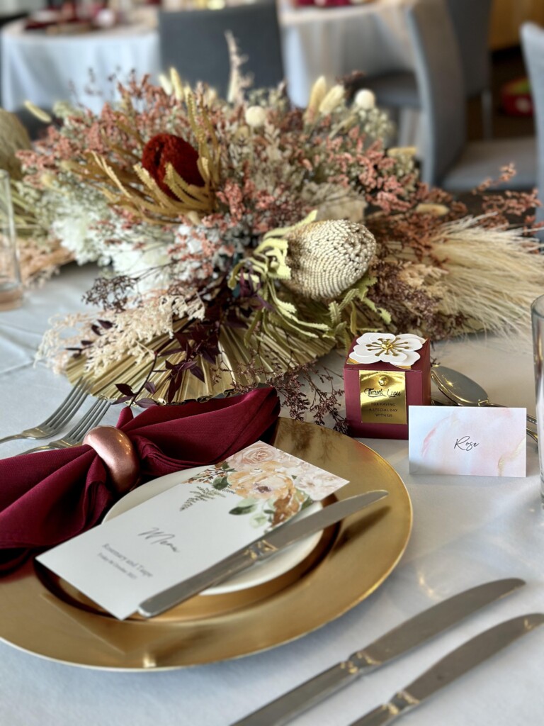 Details from the reception tables, with gold charger plates, floral stationary, maroon napkins and native floral arrangements.
