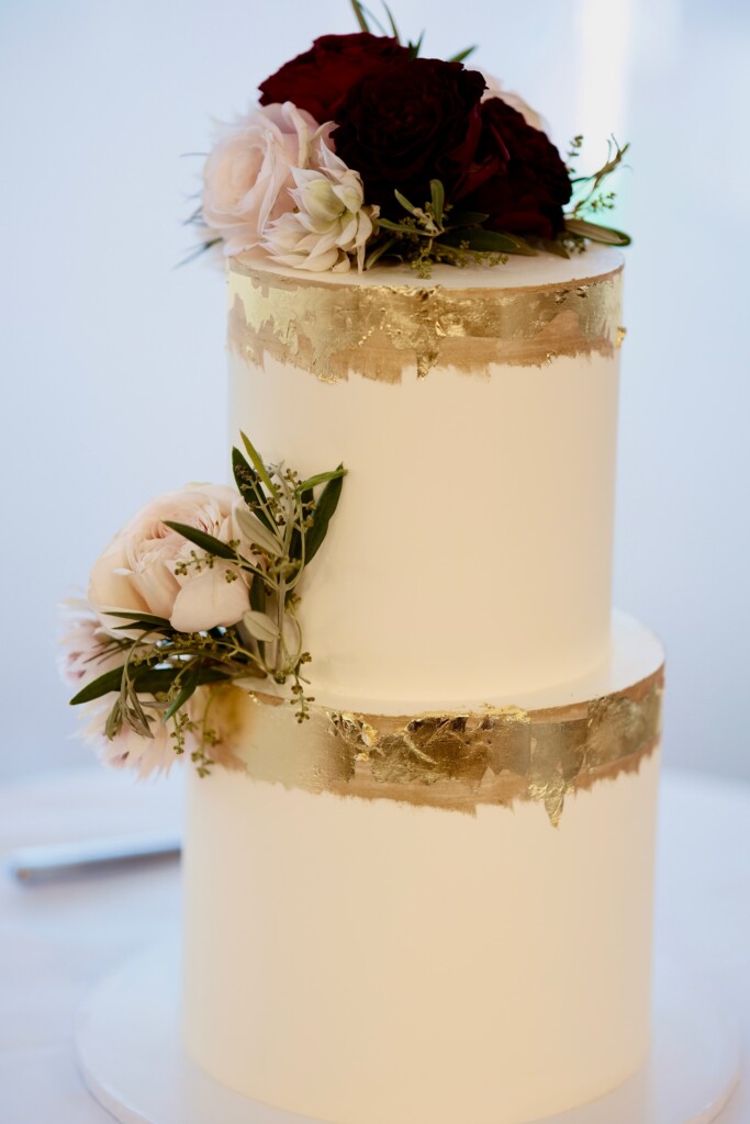 The wedding cake is two tier, with gold leaf details and fresh roses.