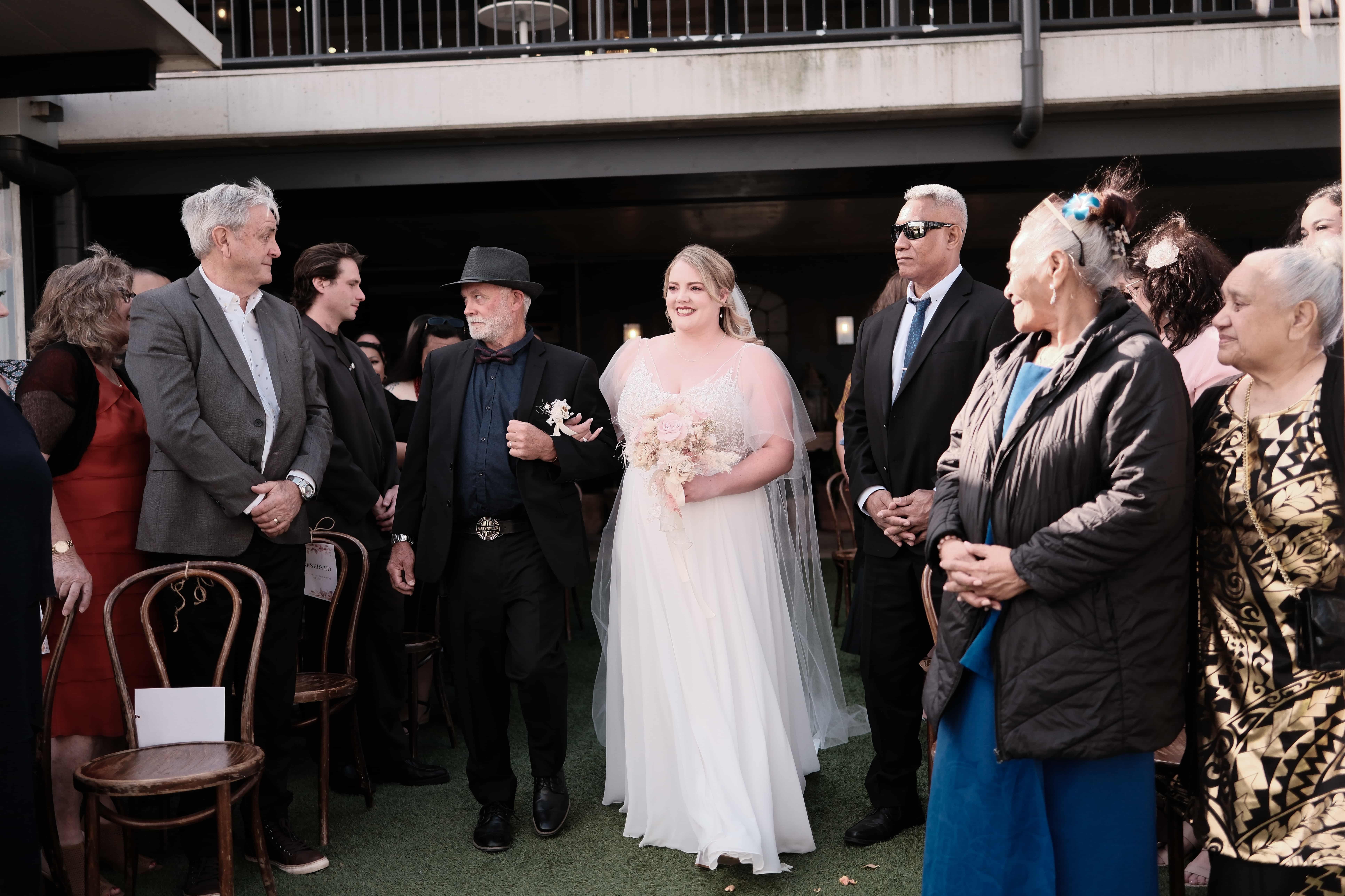 Rose the bride walks down the aisle with her father, as guests stand nearby