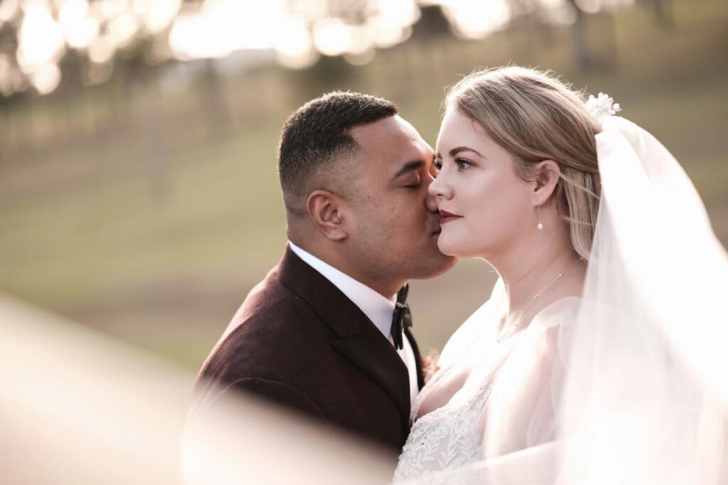 Rose and Taape stand in the parklands as Taape kisses her cheek