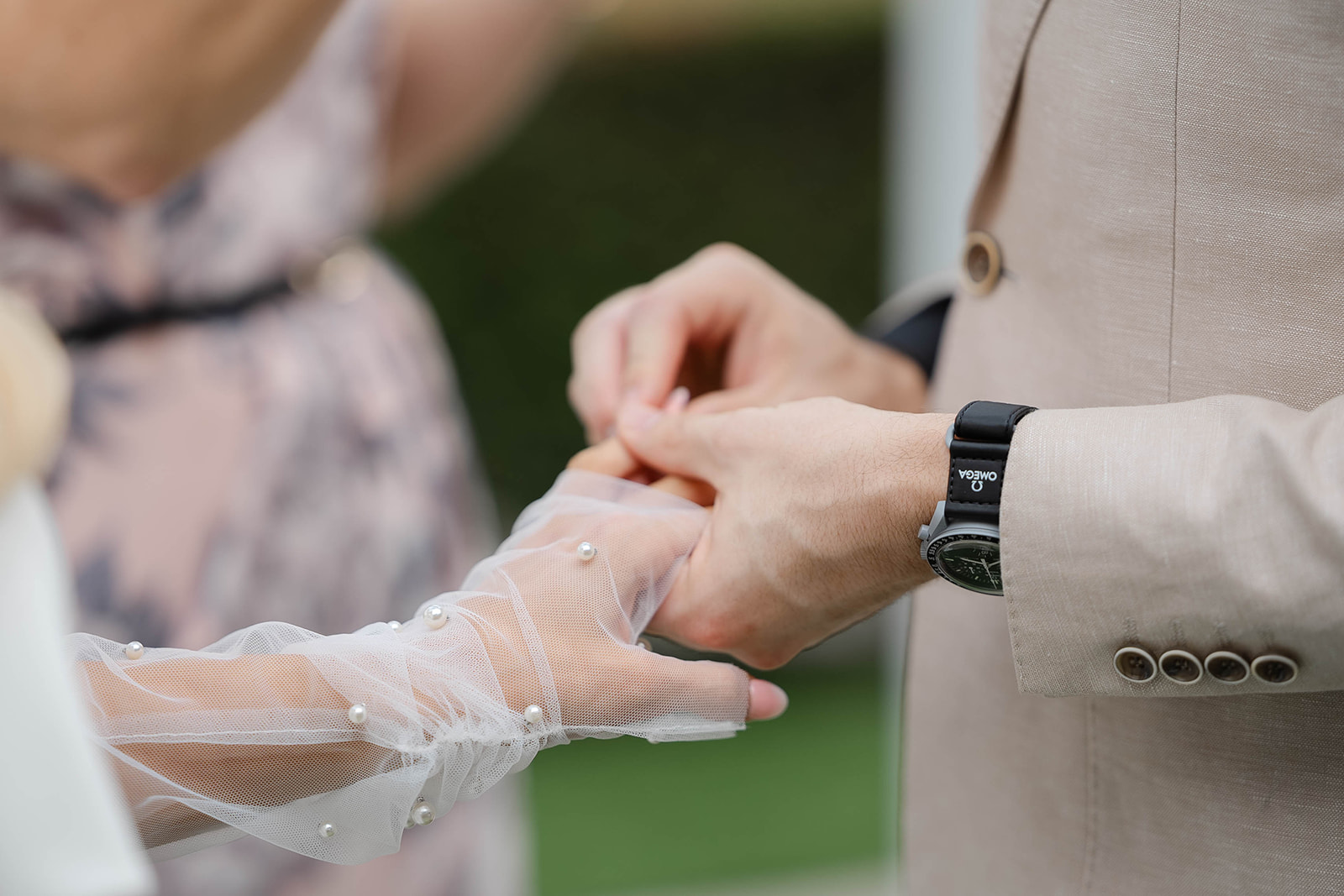 A close up photo of the groom placing the wedding band onto the bride who wears tulle gloves adorned with pearls.