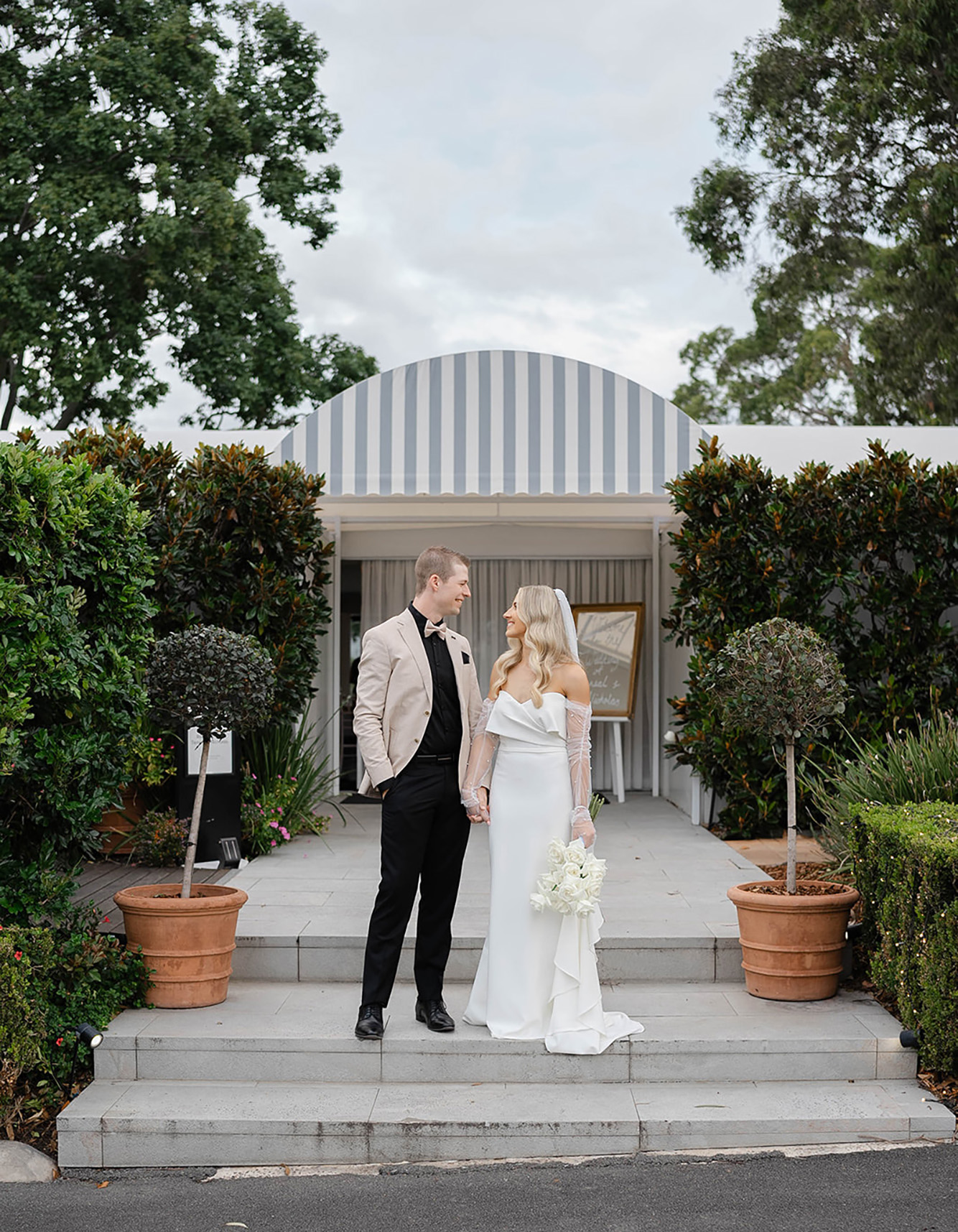 The bride and groom stand together in front of the Garden Marquee, looking at each other.