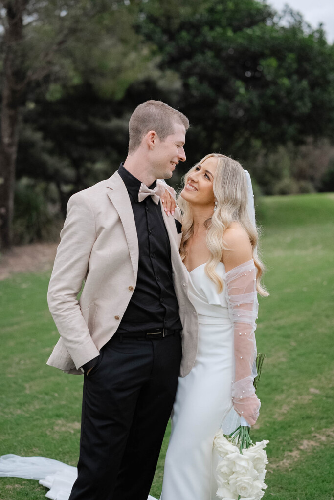 Bride and groom stand looking at each other in the parklands.