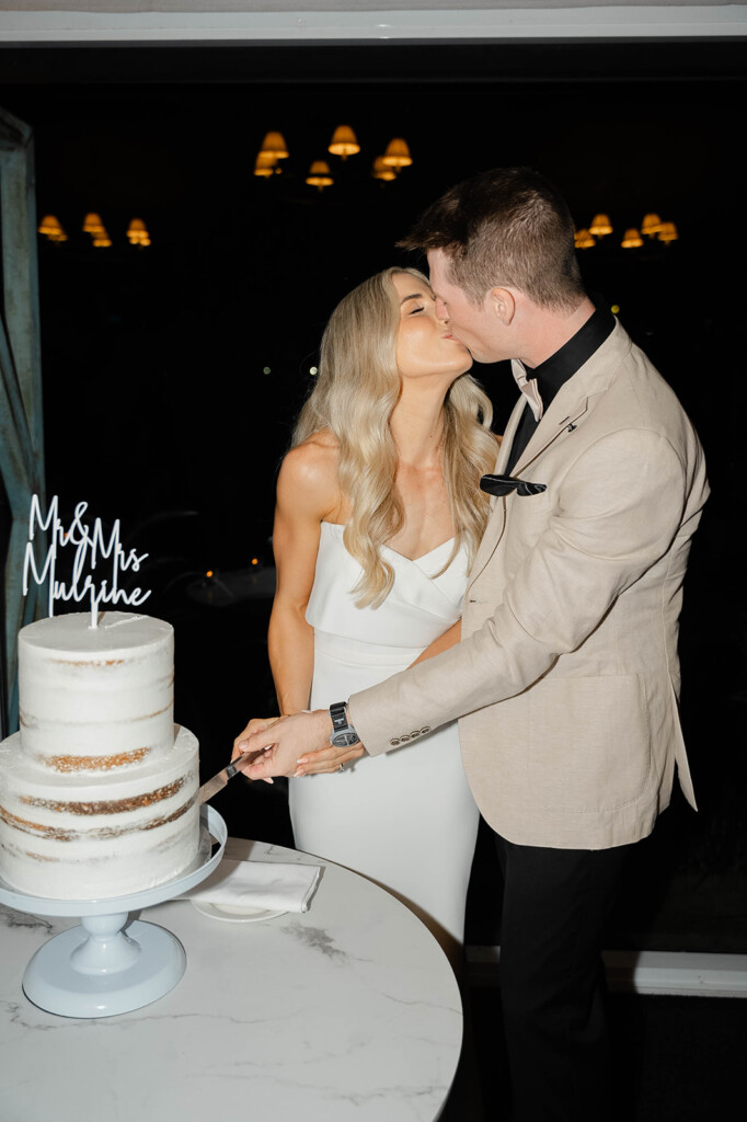 Bride and groom kiss as they cut their cake.